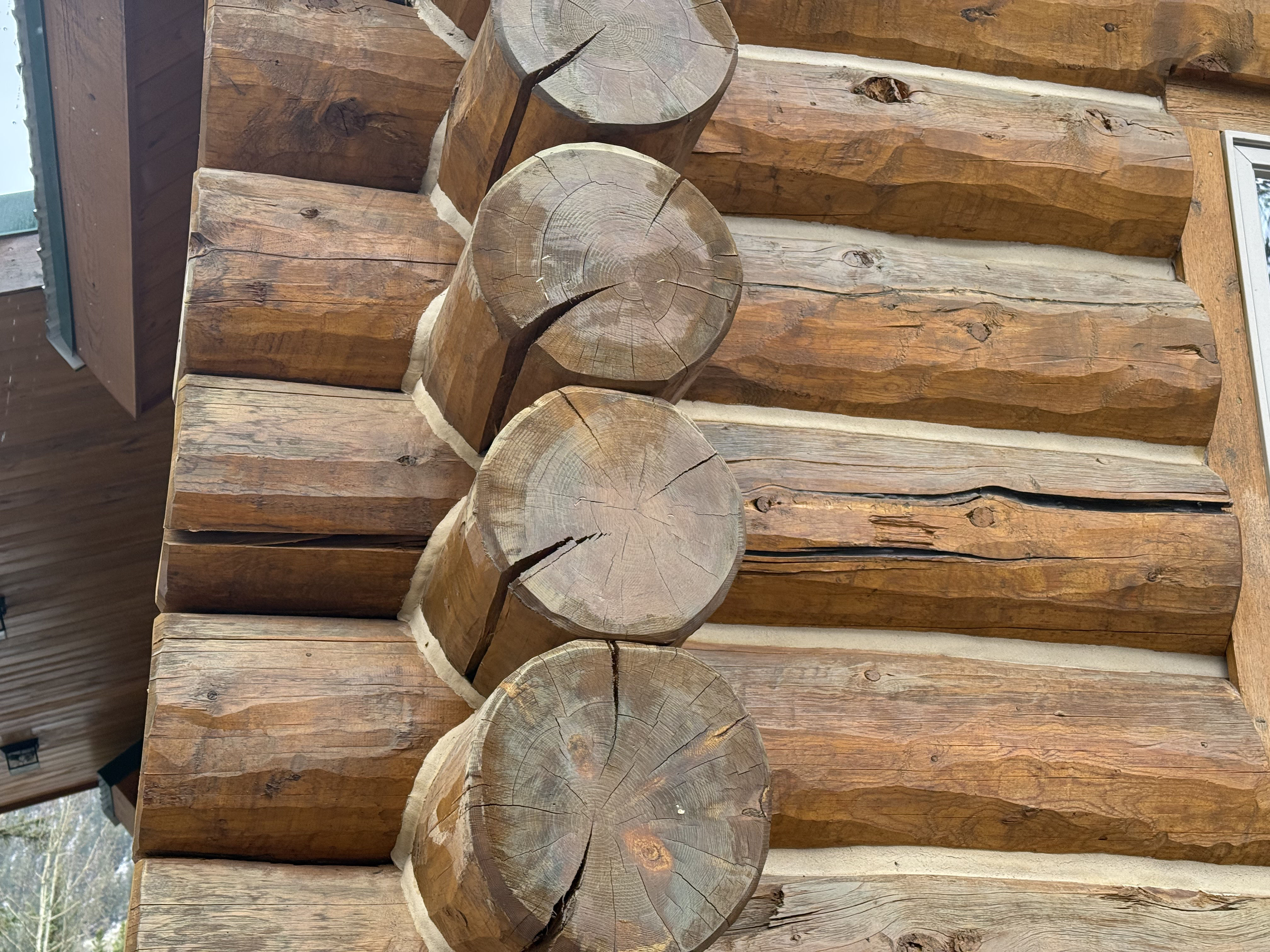 Log cabin chinking maintenance showing natural wood checking and cracking that requires professional attention